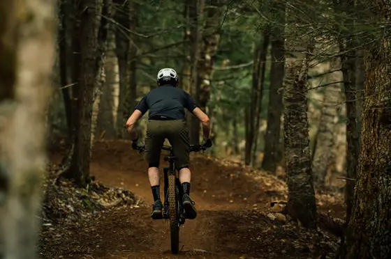 Ciclista de espaldas bajando por un sendero de tierra en el bosque